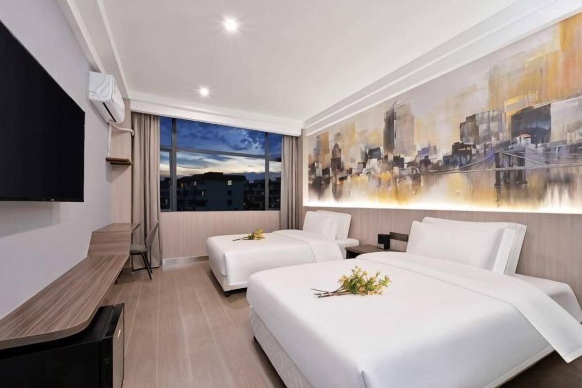 Habitación de hotel con dos camas, un televisor de pantalla plana, un escritorio y un cuadro grande con una vista urbana.