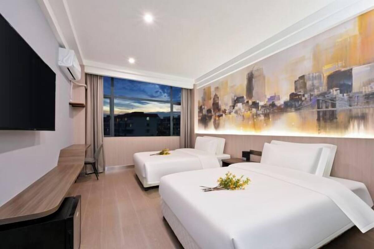 Una habitación de hotel moderna con dos camas, un televisor de pantalla plana, un escritorio de madera y un cuadro abstracto grande en la pared.