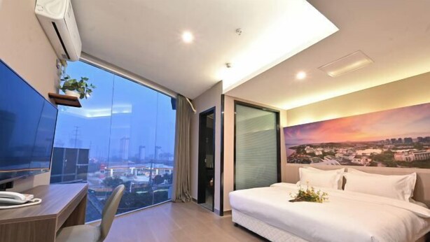 Una habitación de hotel moderna con una cama grande, un escritorio con silla, un ventanal con vista a la ciudad y un cuadro en la pared.