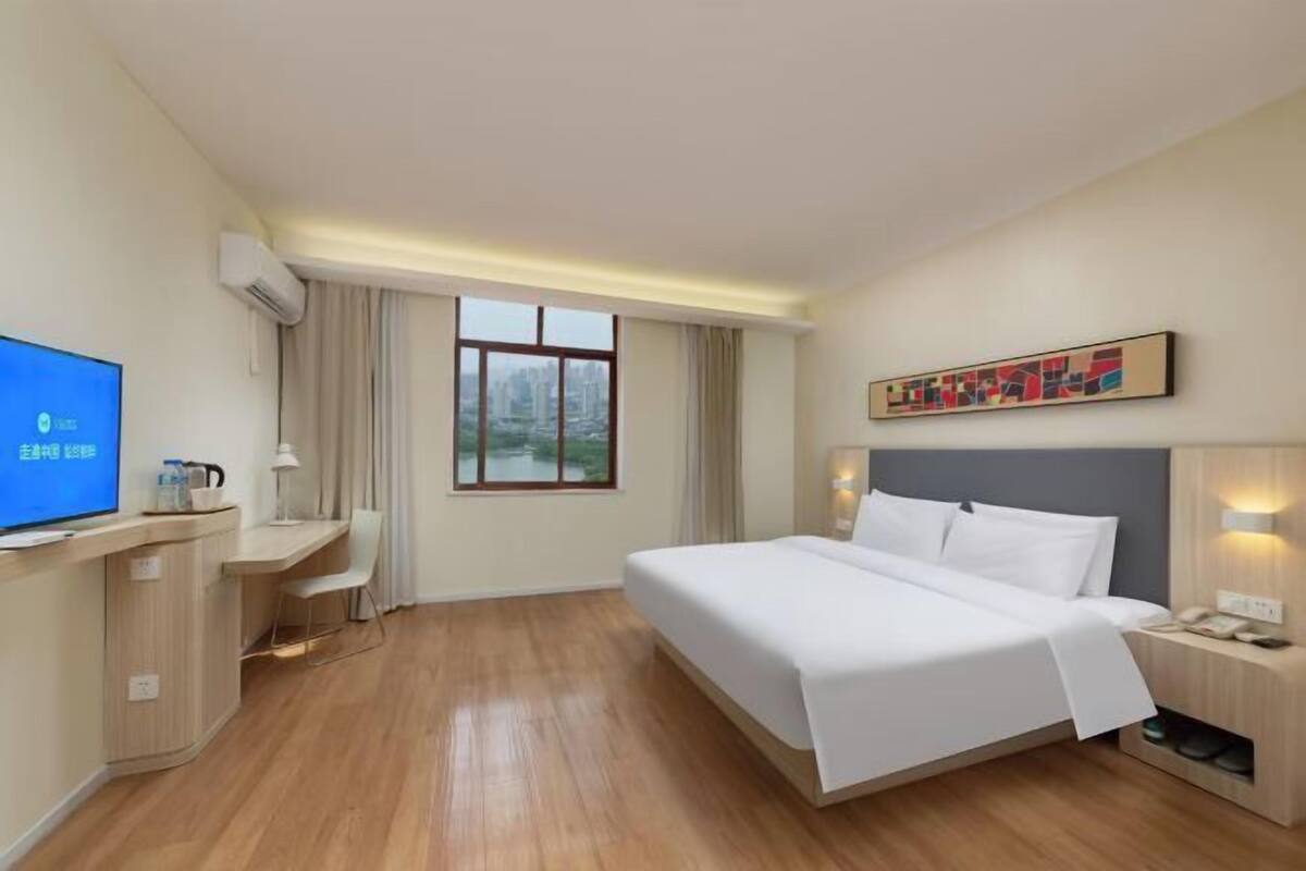 Habitación de hotel con cama, escritorio, televisión y ventana con vista a edificios.