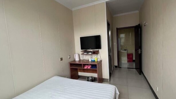 Une chambre d’hôtel avec un lit, un téléviseur posé sur un meuble, un petit bureau avec une chaise et une porte donnant sur une autre pièce.