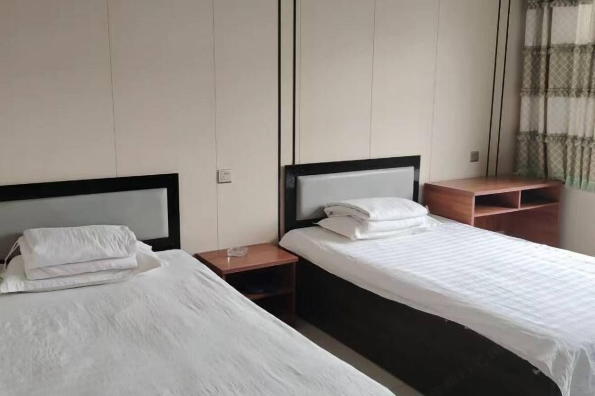 Une chambre d’hôtel avec deux lits, chacun doté d’une table de chevet en bois et d’un oreiller blanc.
