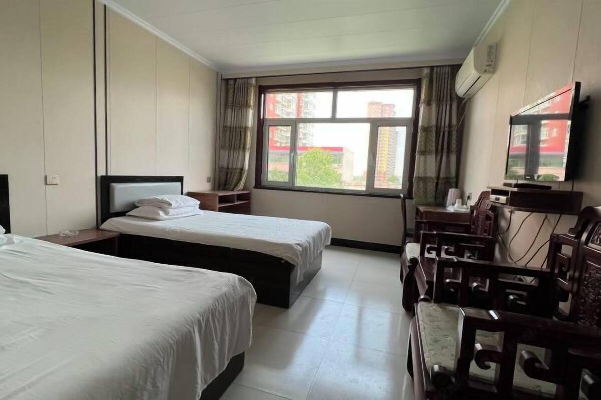 Une chambre d’hôtel avec deux lits, un bureau avec une chaise, une télévision et une fenêtre avec des rideaux.