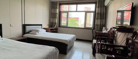 A hotel room with two beds, a desk with a chair, a TV, and a window with curtains.