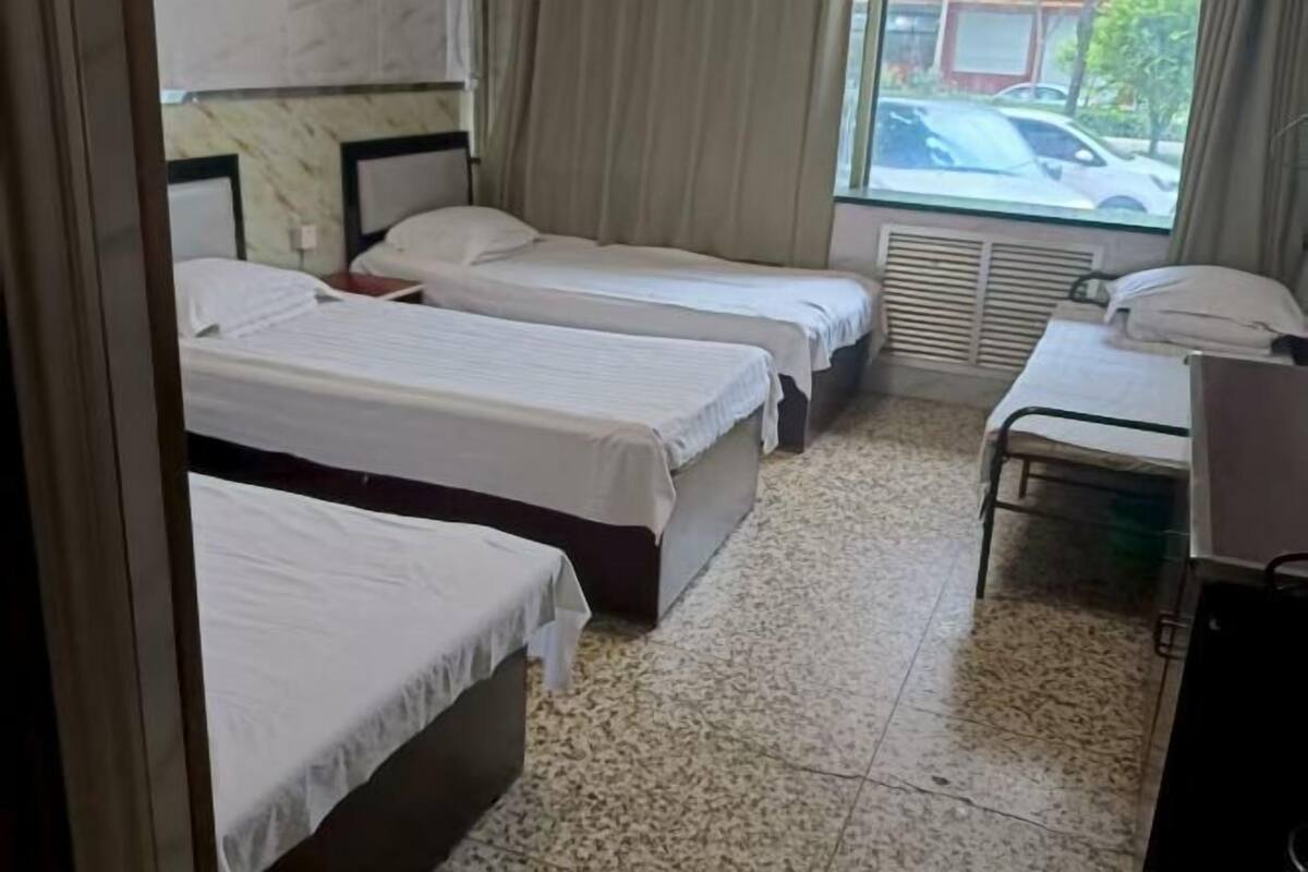 Une chambre d’hôtel avec trois lits simples, une petite table et une fenêtre donnant sur l’extérieur.