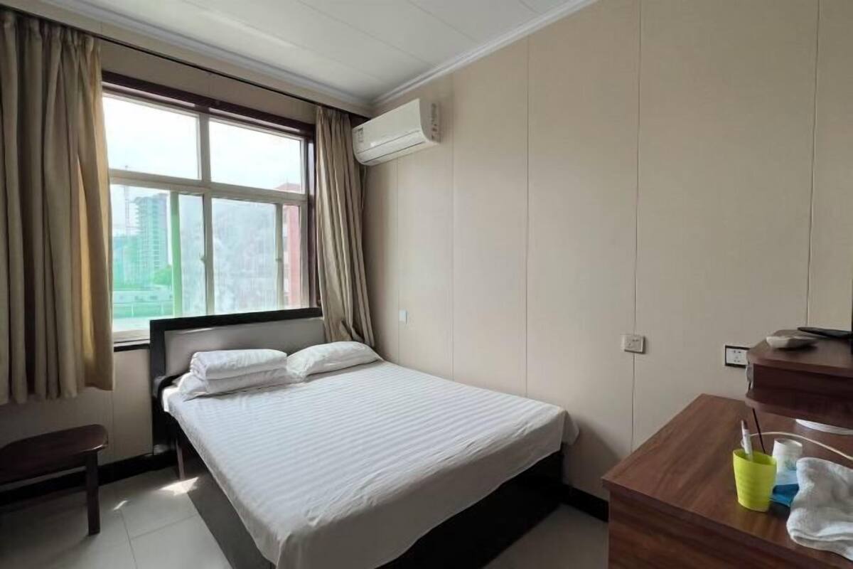 Une chambre d’hôtel équipée d’un lit, d’un bureau, d’un miroir, d’un climatiseur et d’une fenêtre avec des rideaux.