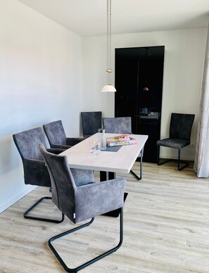 A modern dining area with a rectangular table, grey upholstered chairs, a hanging pendant light, and a black cabinet in the background. - Apartment 'Mühlentrift 32, 6' with Balcony and Wi-Fi (Cuxhaven)