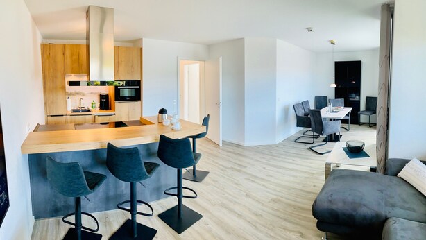 Une cuisine moderne dotée d’un îlot central, de tabourets de bar, d’un coin repas avec une table et des chaises, et d’un espace de détente avec un canapé.
