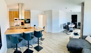 A modern kitchen with a central island, bar stools, a dining area with a table and chairs, and a living area with a sofa. - Apartment 'Mühlentrift 32, 6' with Balcony and Wi-Fi (Cuxhaven)
