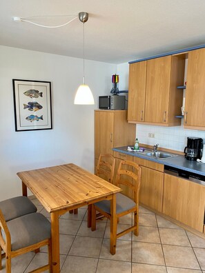 A kitchen with wooden cabinets, a dining table with chairs, a microwave, and a framed fish artwork on the wall.