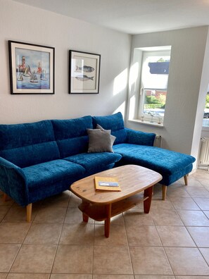 A blue sectional sofa, a wooden coffee table, and two framed pictures on the wall.
