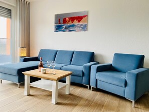 A blue sofa, a wooden coffee table, and a painting on the wall. - Apartment 'Duhner Allee 10, Litfaß 17' with Balcony and Wi-Fi (Cuxhaven)