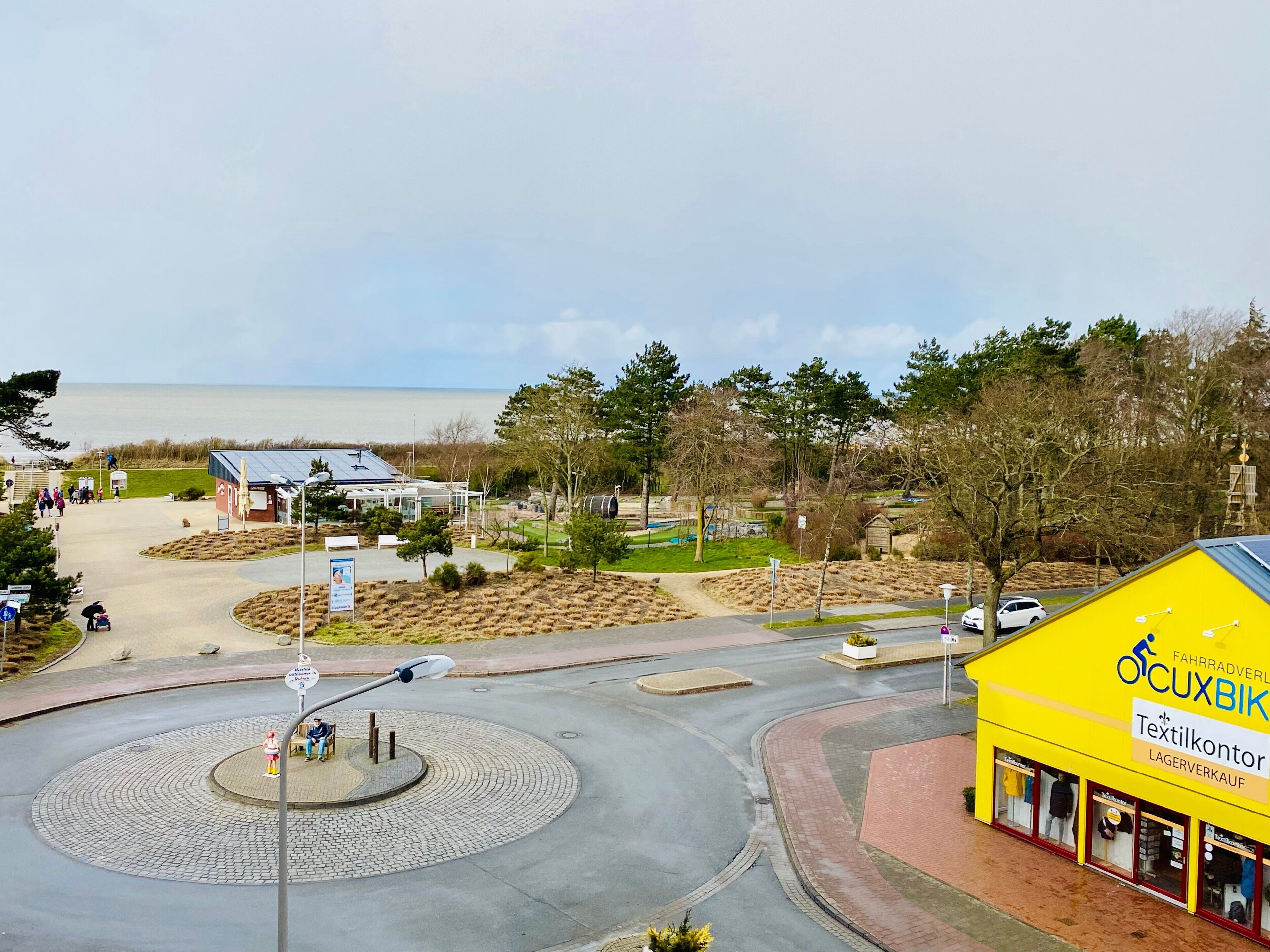 A roundabout with a central island, a yellow building with signage, and a body of water in the background.