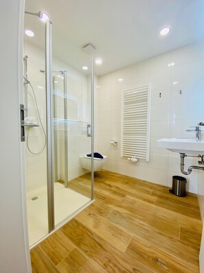 Un baño moderno con cabina de ducha de vidrio, inodoro, lavabo y radiador.