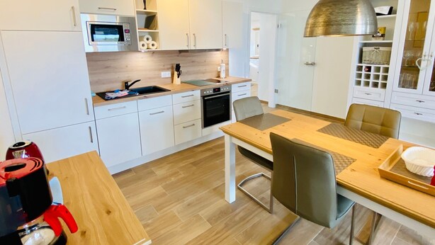 A modern kitchen with white cabinets, a wooden countertop, a built-in oven, and a dining area with a table and chairs. - Apartment 'Duhner Allee 10, Litfaß 17' with Balcony and Wi-Fi (Cuxhaven)