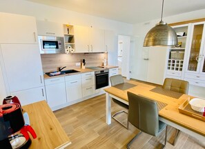 A modern kitchen with white cabinets, a wooden countertop, a built-in oven, and a dining area with a table and chairs. - Apartment 'Duhner Allee 10, Litfaß 17' with Balcony and Wi-Fi (Cuxhaven)