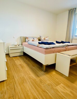 Un dormitorio con cama, mesitas de noche, armario y ventana con cortinas.