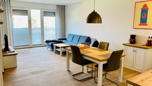 A modern living room with a sofa, dining table, chairs, and a kitchen area with cabinets and appliances. - Apartment 'Duhner Allee 10, Litfaß 17' with Balcony and Wi-Fi (Cuxhaven)
