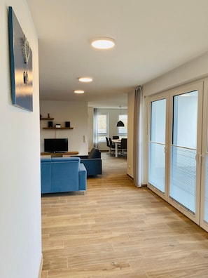 Un salon moderne avec un canapé bleu, un téléviseur à écran plat et un coin repas comprenant une table et des chaises.