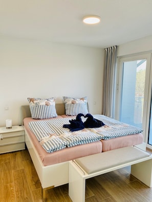 Een slaapkamer met een bed, nachtkastjes, een bankje en een raam met zonwering.