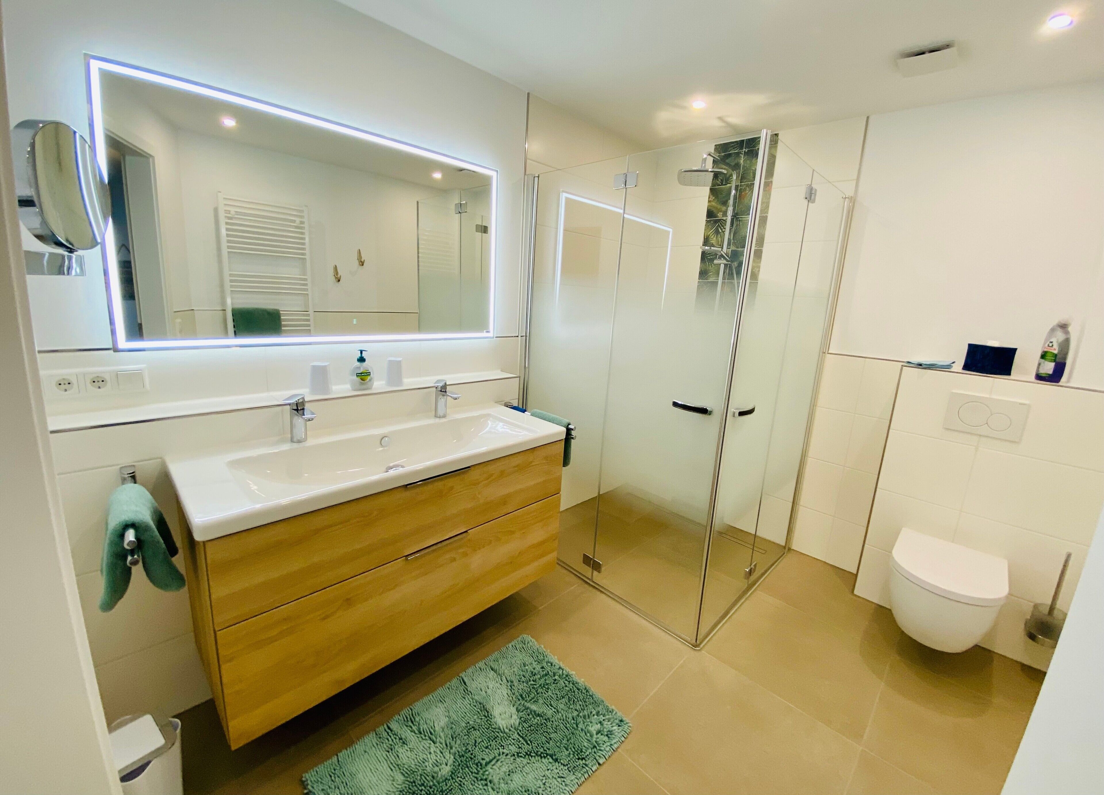 Een moderne badkamer met een grote spiegel, een wastafel, een douche en een toilet.