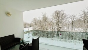 En balkong med möbler i rotting, utsikt över ett snötäckt landskap och en klar himmel.