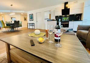 Une cuisine moderne avec des meubles blancs, une hotte noire et un coin repas comprenant une table et des chaises en bois.