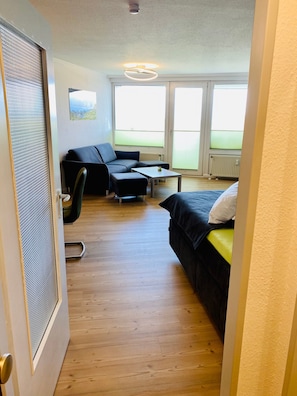 Una habitación con sofá, una mesita, cama y ventanas amplias.