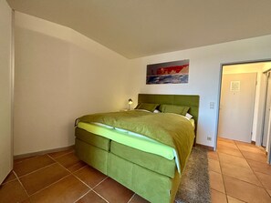 Un dormitorio con una cama verde, una mesita de noche con lámpara y un cuadro en la pared.