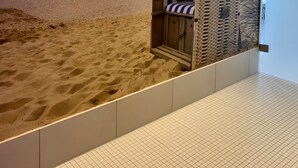 Ett rum med strandtema, komplett med ett sandtäckt golv, en randig strandstol och en väggmålning som föreställer havet.