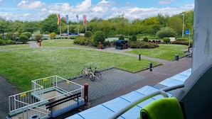 A view from a balcony overlooking a courtyard with a small green structure, bicycles, and flags. - Apartment '109' with Balcony and Wi-Fi (Cuxhaven)