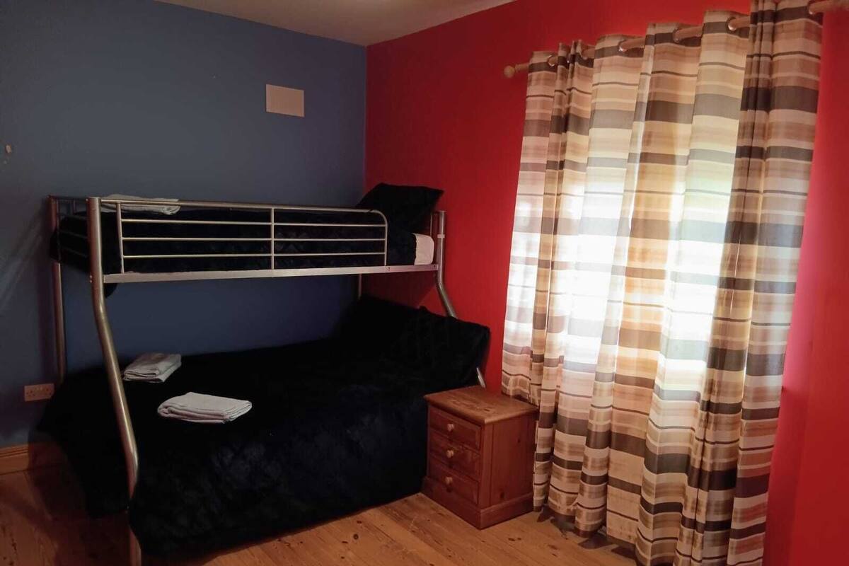 A room with a bunk bed, a small wooden cabinet, and a window with striped curtains.