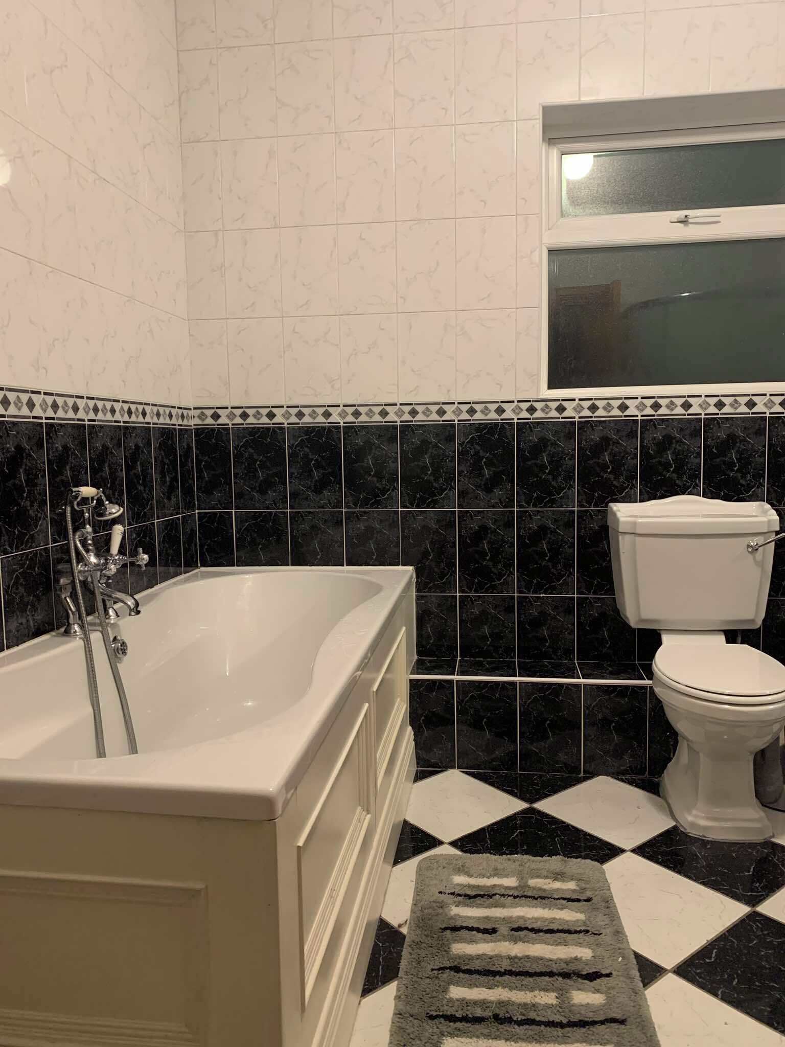 Ein Badezimmer mit Badewanne, Toilette und einem Fenster über der Toilette.