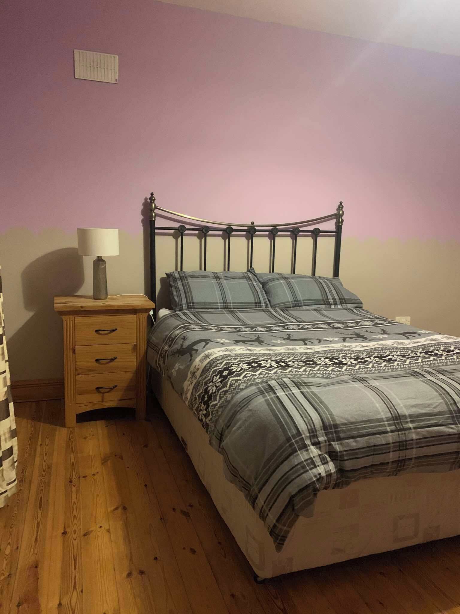 A bedroom with a bed, a nightstand, a lamp, and a wooden dresser.