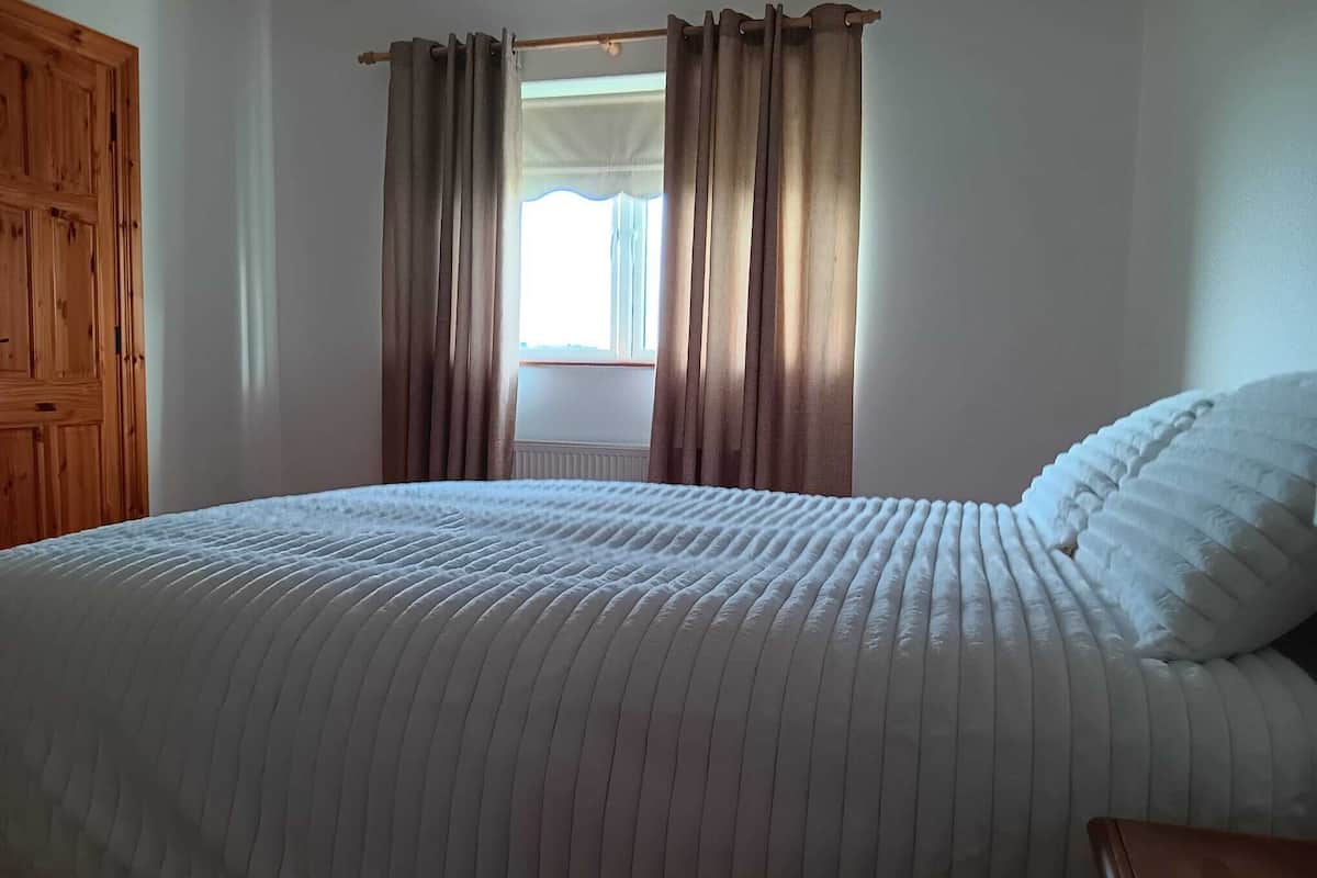 A bedroom with a bed, wooden wardrobe, and curtains.