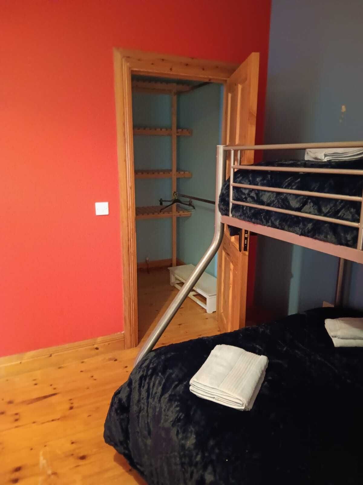 A room with a bunk bed, wooden flooring, a door leading to a hallway, and a small white stool.