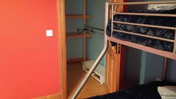A room with a bunk bed, wooden flooring, a door leading to a hallway, and a small white stool.