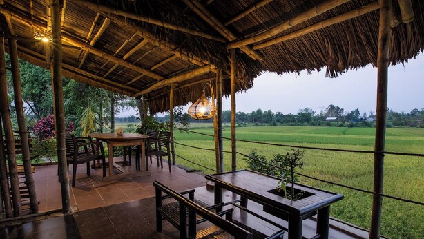 A covered outdoor seating area with a table and chairs, overlooking a green field. - Two independents BR in a pristine area in Hoi An (Thành phố Hội An)