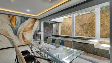 A modern dining area with a glass table, cushioned chairs, a stone accent wall, and a large abstract painting.