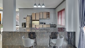 A modern kitchen with a marble island, two bar stools, and a dining area with a view of the outdoors. - Villa Master Residance - Denpasar (Denpasar)