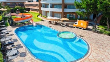 A swimming pool with lounge chairs and a lifeguard stand, surrounded by a tiled walkway and a building with balconies.