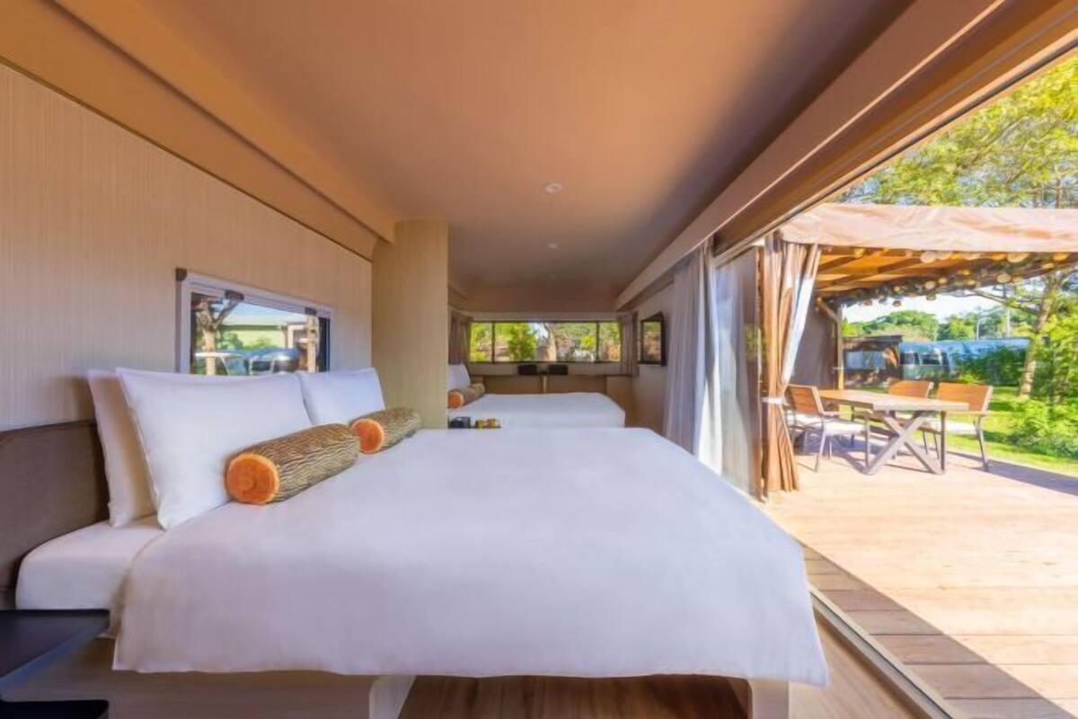 Ein modernes Hotelzimmer mit einem großen Bett, Blick auf die Außenveranda und ein Fenster mit Blick auf die Grünanlage.