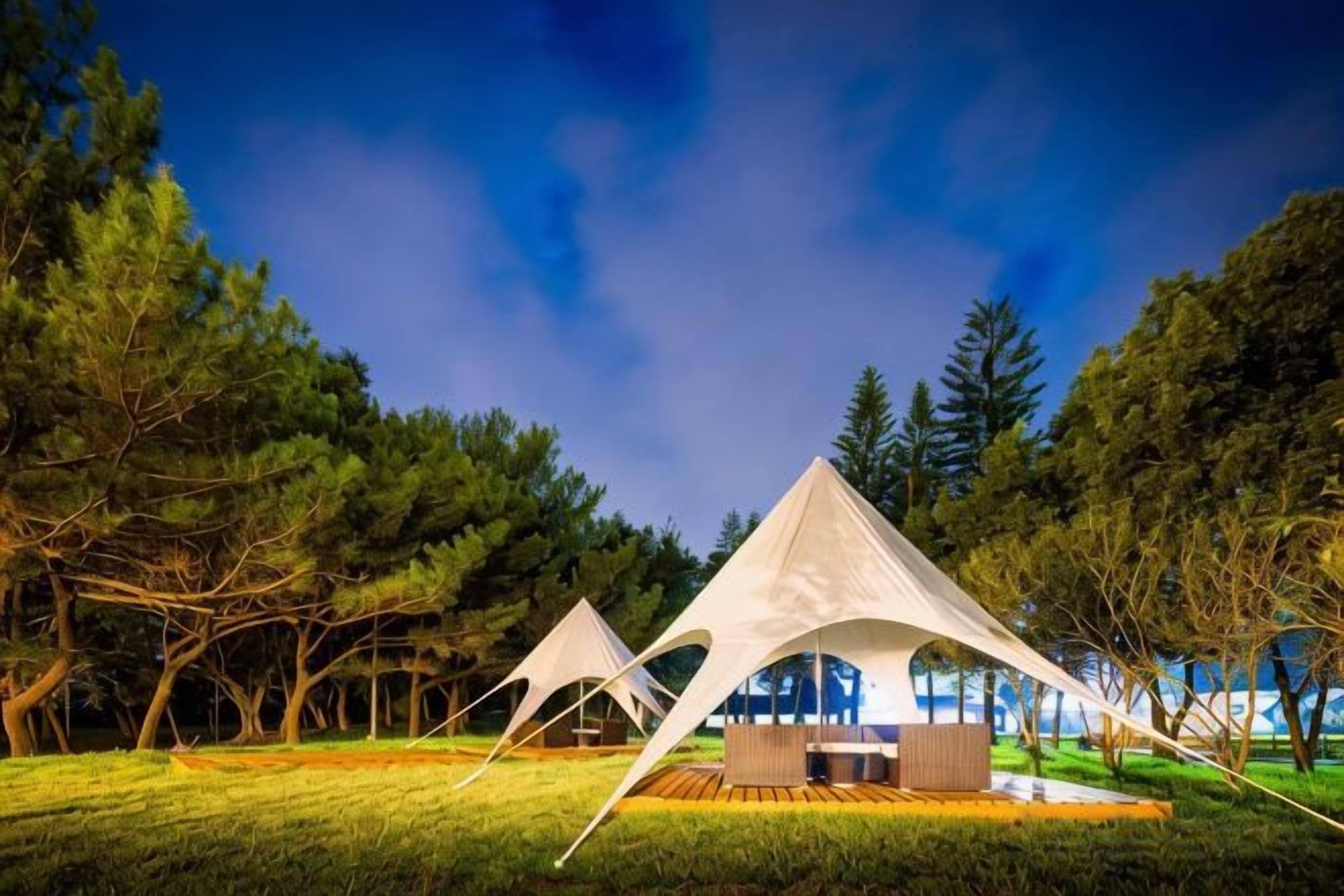 A tented accommodation with a dining area, surrounded by trees.