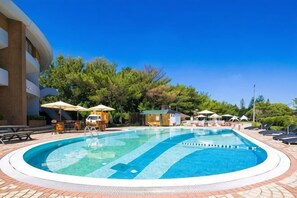 A pool with lounge chairs and umbrellas, surrounded by trees and a building.