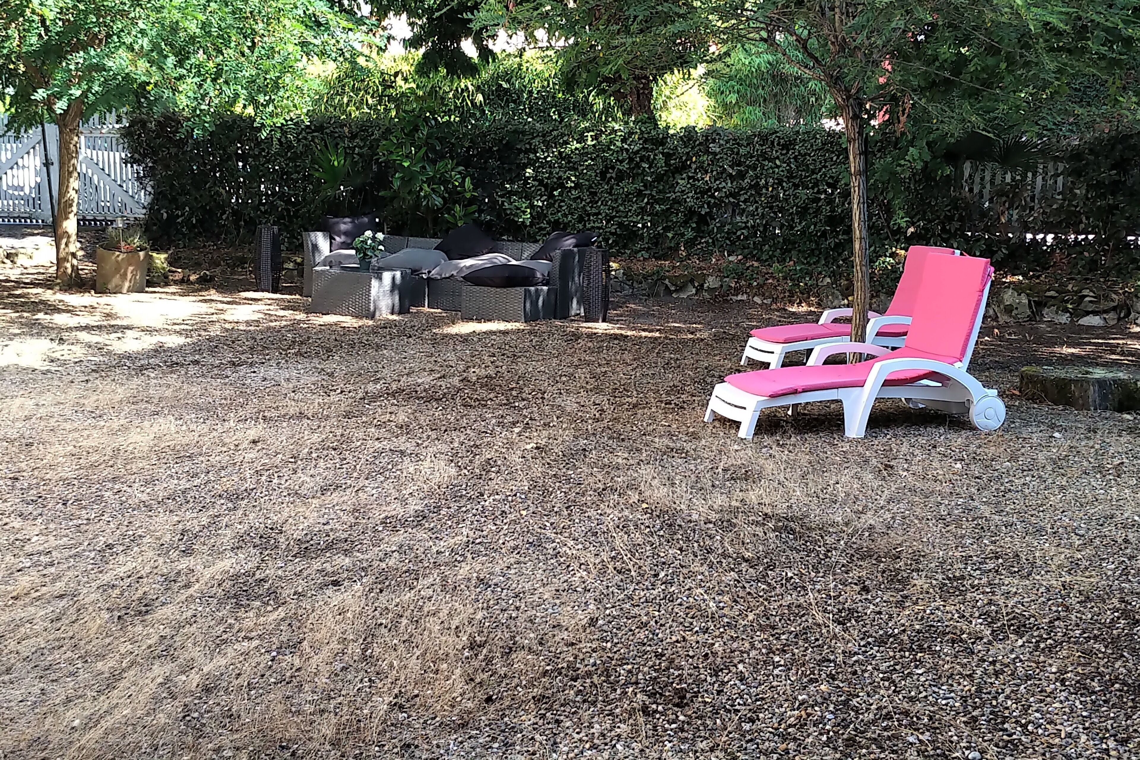 A garden area with a seating arrangement including a white and pink lounge chair, a wicker sofa, and a small table with a potted plant.