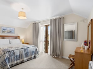 Un dormitorio con cama, lámpara de noche, cortinas, cómoda de madera, espejo y ventana.