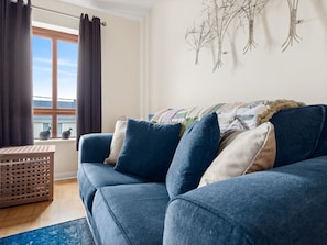 A blue sofa with cushions, a wooden crate, and a window with curtains.