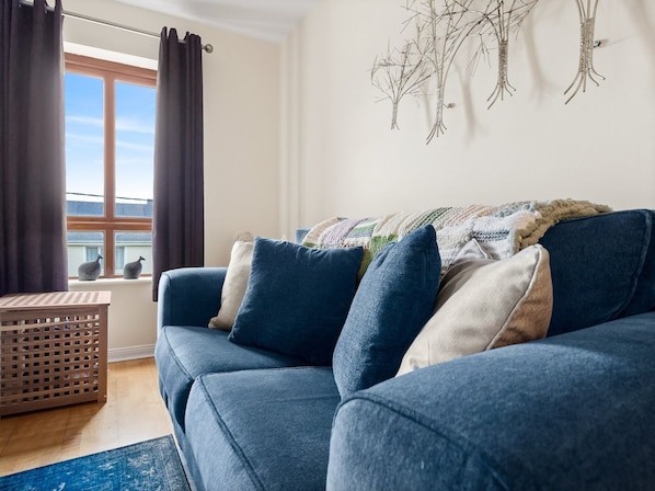 A blue sofa with cushions, a wooden crate, and a window with curtains.