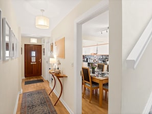 A hallway leading to a dining area with a wooden table and chairs, a rug on the floor, and a door at the end.