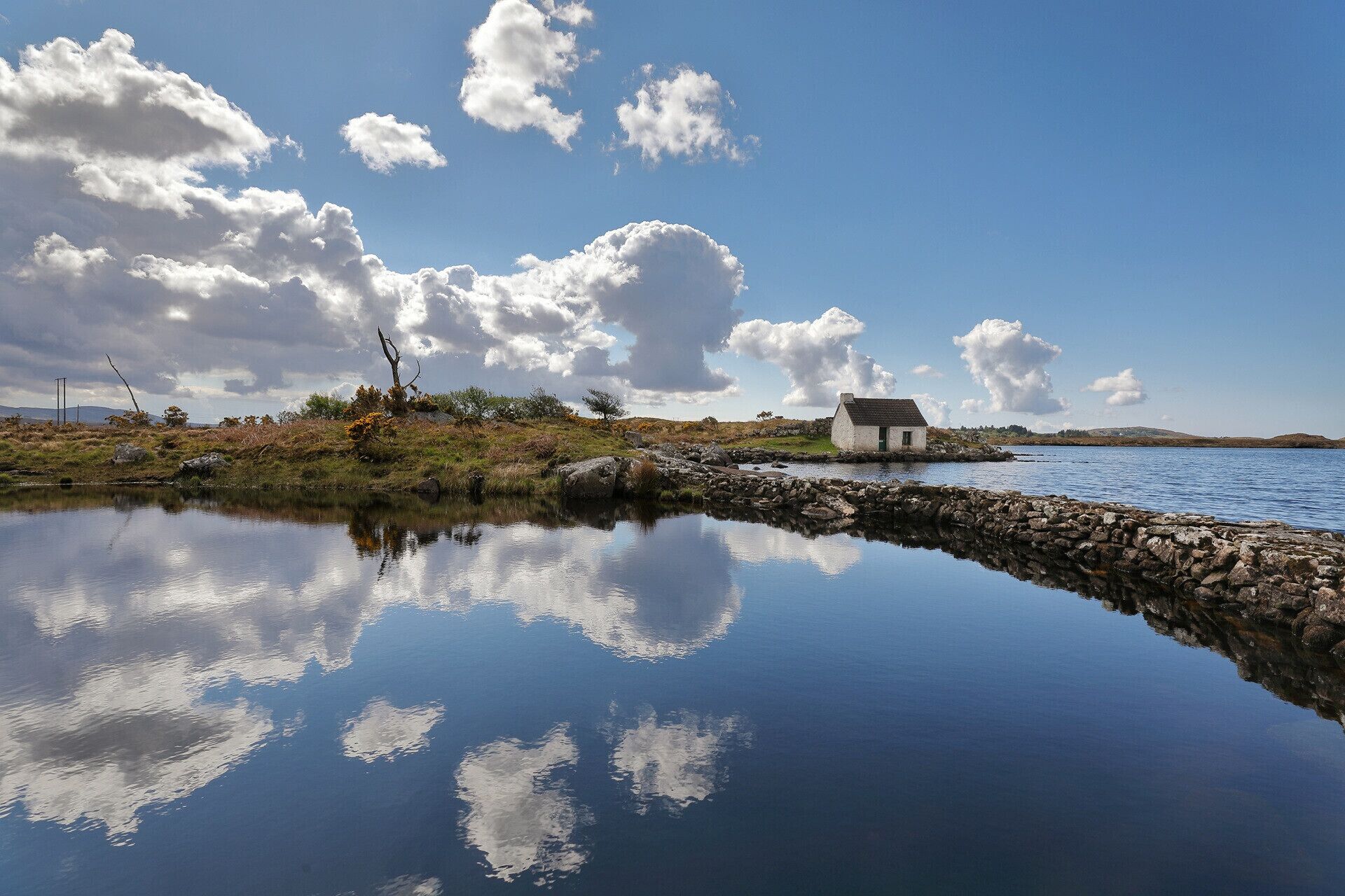A calm lake with a small house on a rocky shore, surrounded by natural landscape and clear skies.